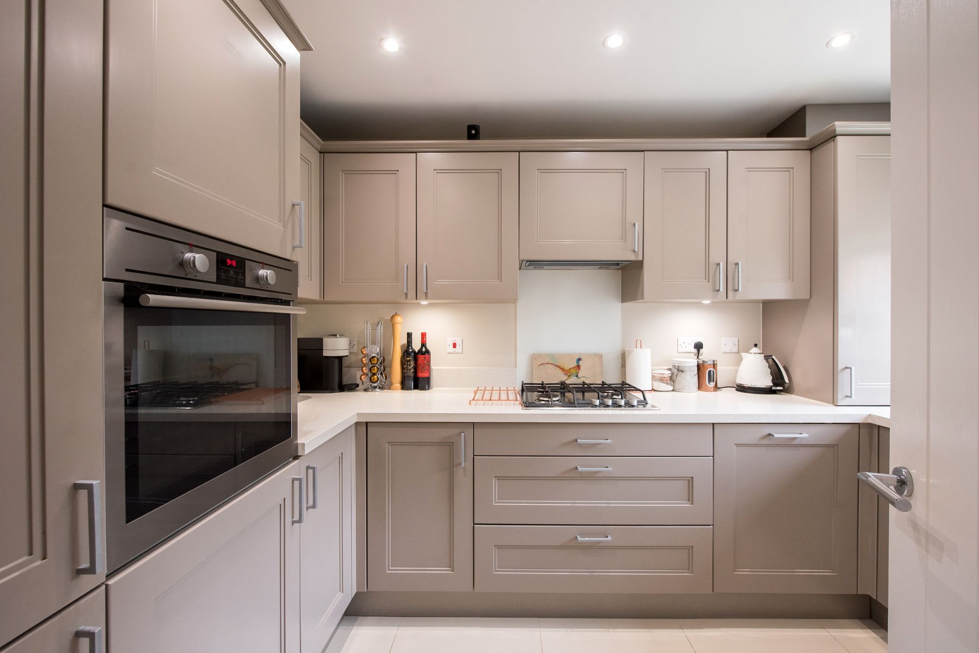 A small truffle taupe shaker style kitchen with custom fitted cabinets in a cozy home interior.