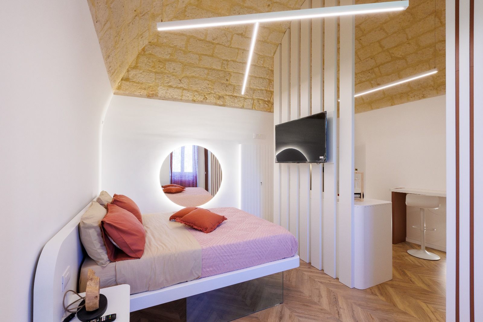 Camera da letto con letto, TV, specchio e soffitto in legno. Caratterizzata dai colori bianco e pesca.