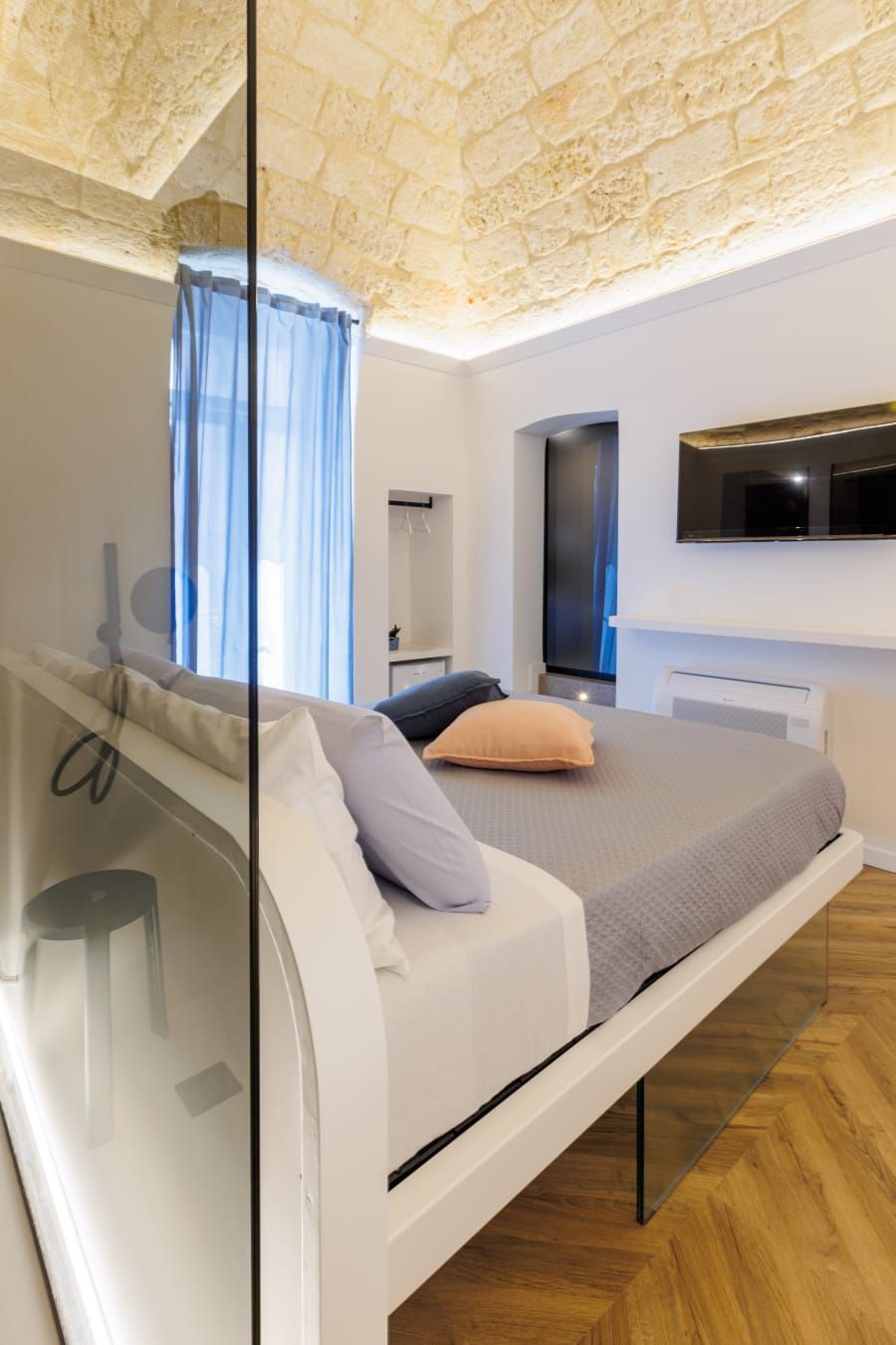 Camera da letto moderna con letto sospeso, soffitto in pietra e parete divisoria in vetro.