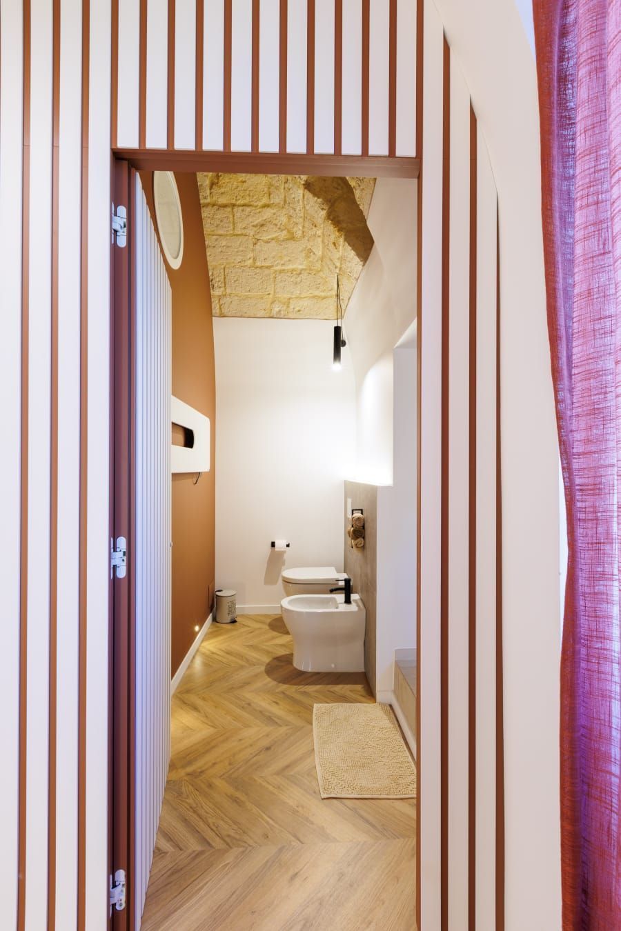 Interno del bagno: porta con parete a strisce verticali che conduce al water, al bidet e al soffitto strutturato.