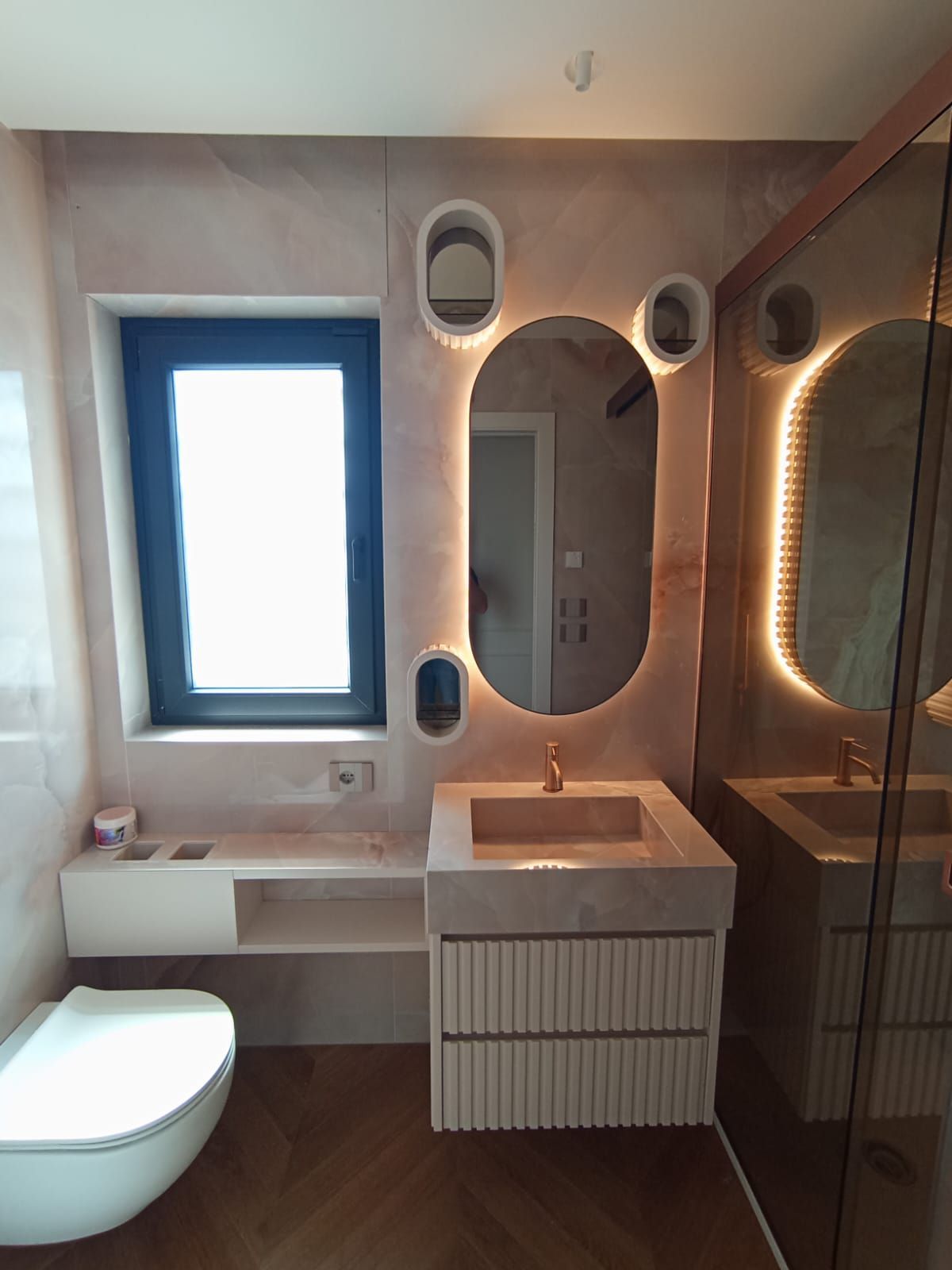 Bagno con specchio ovale con illuminazione a LED, lavandino, WC e doccia.
