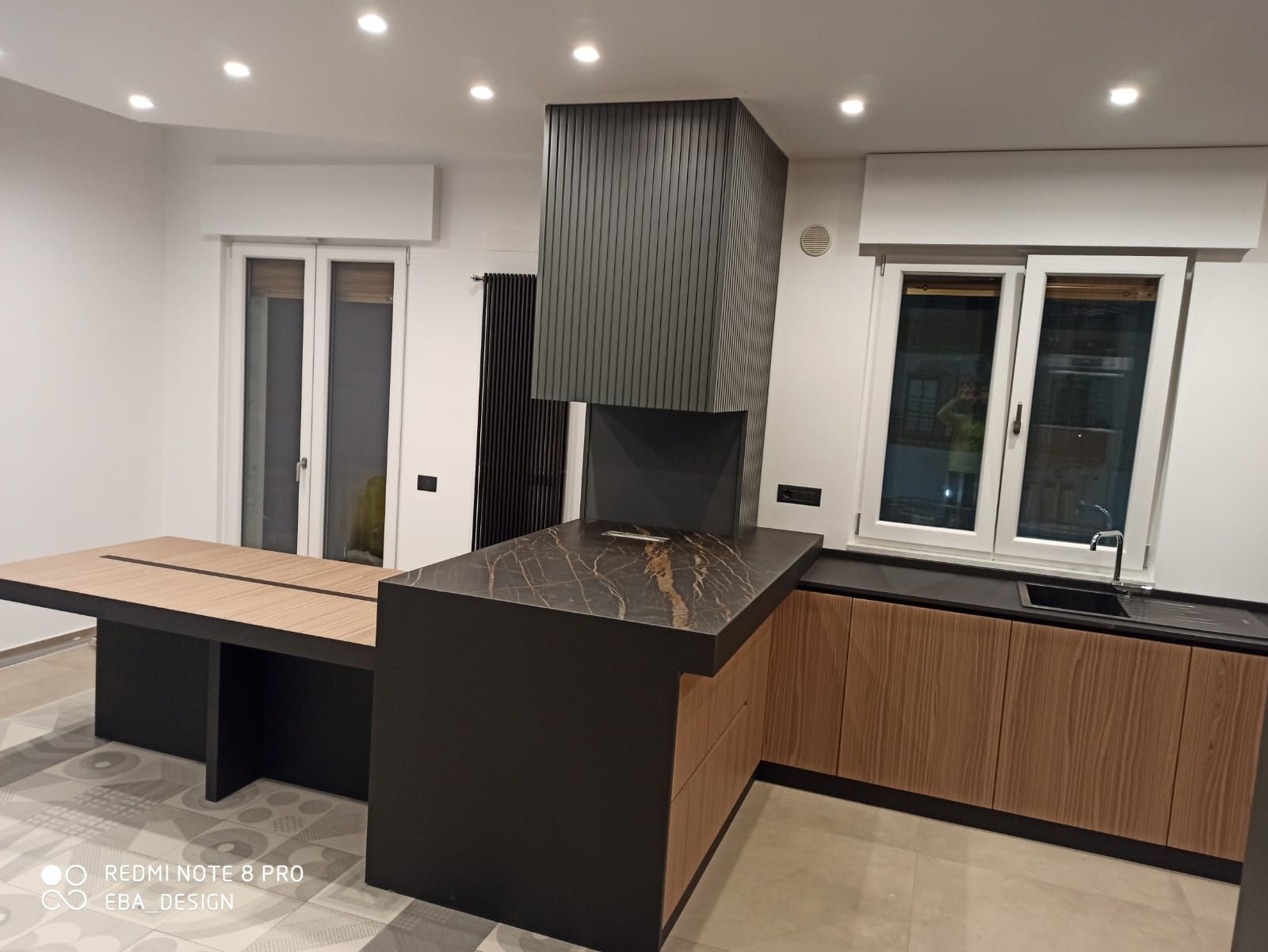 Cucina moderna con mobili scuri, cappa con motivi e tavolo che si estende dall'isola.