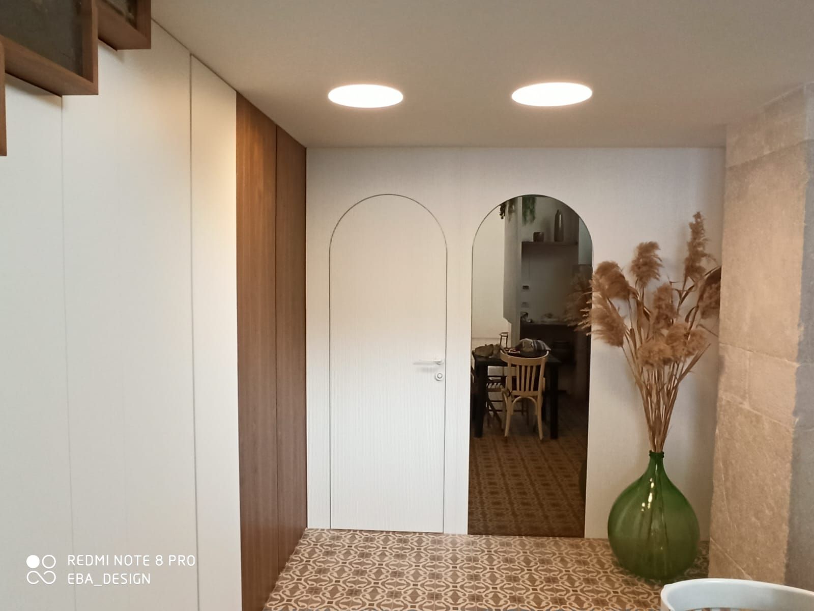 Vista interna: porta ad arco bianca, pavimento in piastrelle decorate, vaso con piante secche.