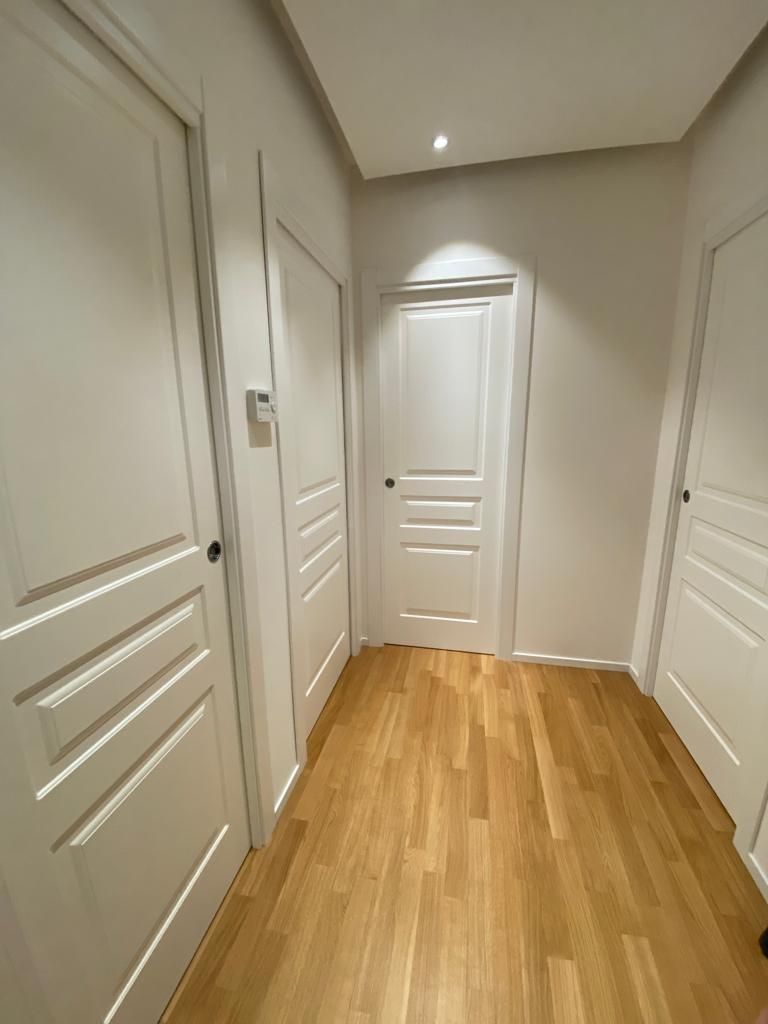 Corridoio stretto con tre porte bianche e pavimento in legno.