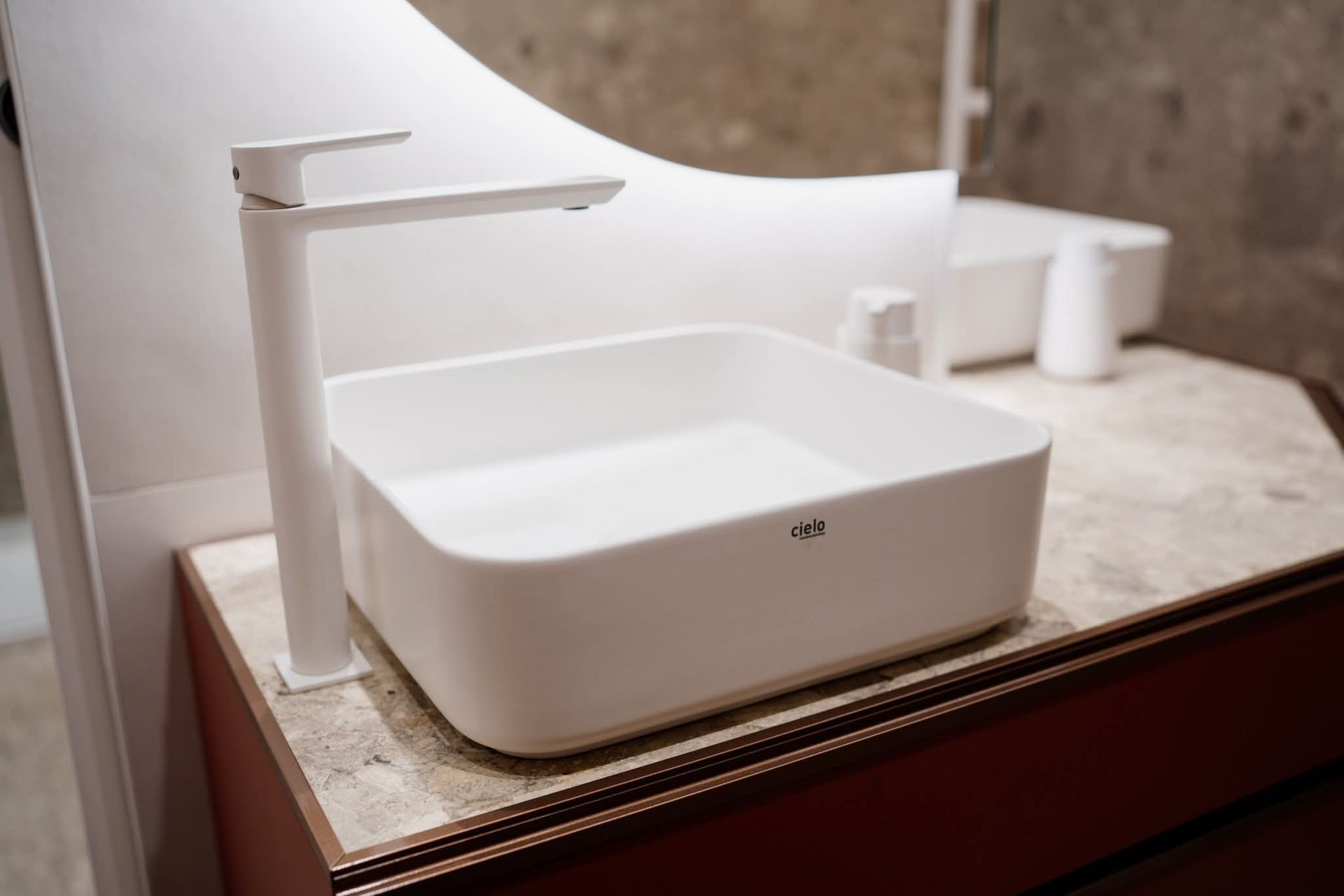 Lavandino e rubinetto bianchi su un mobiletto marrone in un bagno.