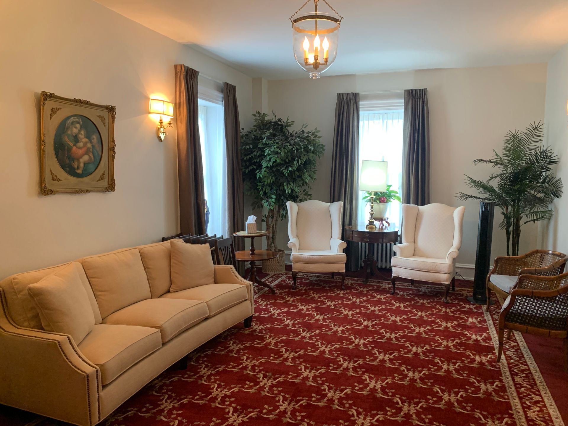 A formal living room with cream furniture, red patterned rug, and wall art.