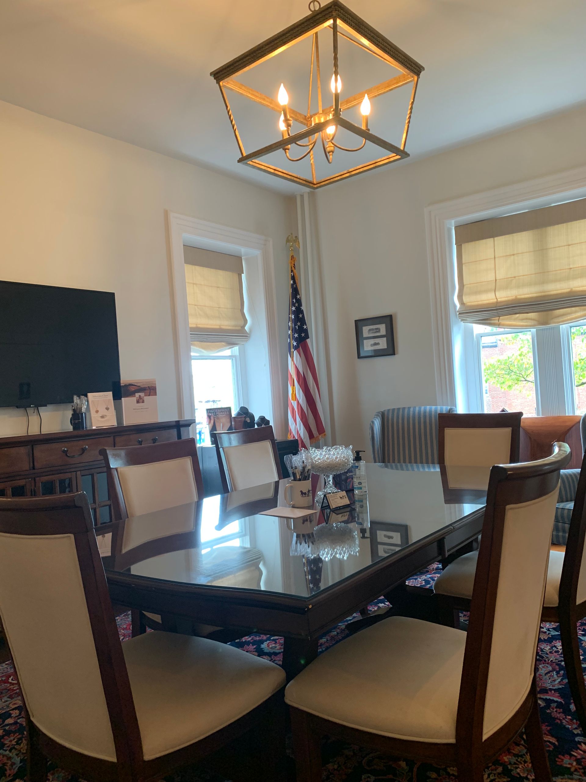 Formal dining room with dark table, cream chairs, chandelier, and American flag.