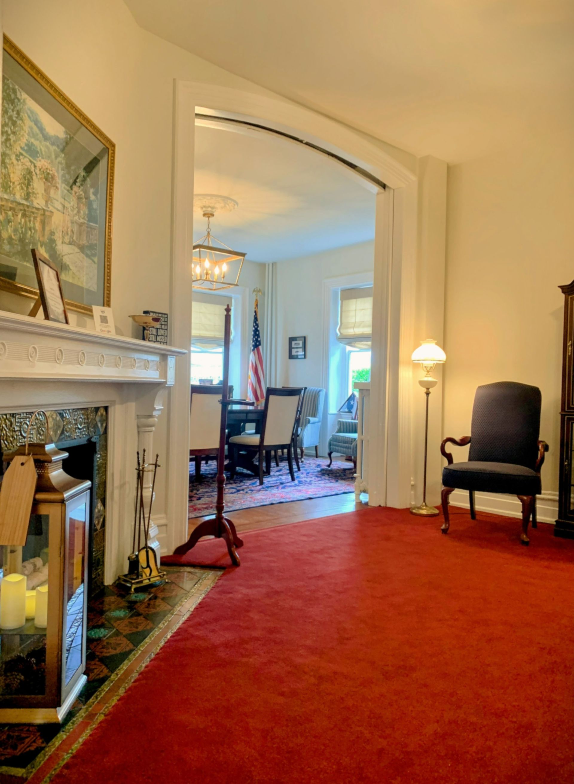 Red-carpeted room with an arched doorway leading to a dining room with a chandelier and American flag.