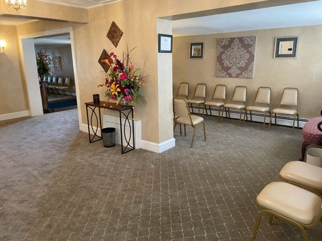 Interior view of a waiting area with chairs, floral arrangement, and a doorway leading to another room.