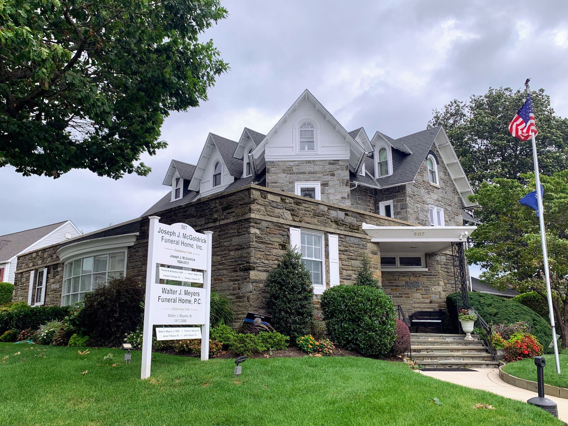 Stone building with multiple gabled roofs, sign, American flag on cloudy day.