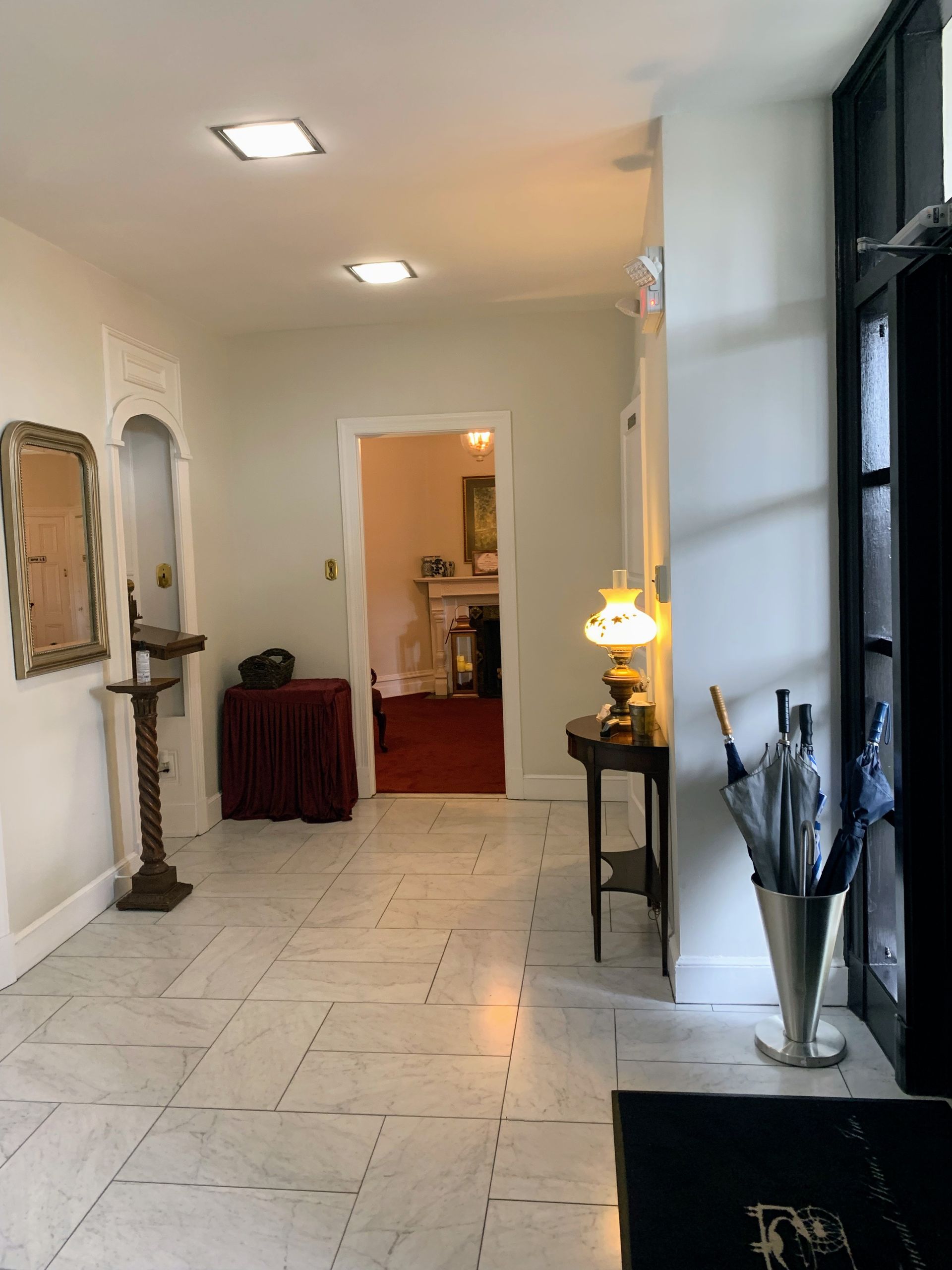Hallway with marble floors, arched doorway, table with lamp, and umbrella stand.