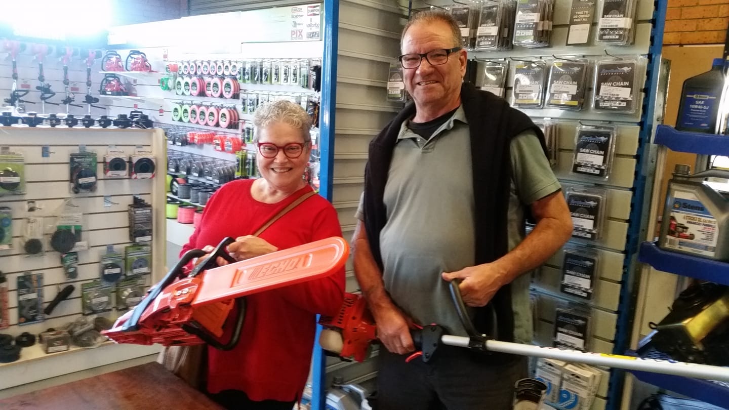 Happy Customers Holding A Chainsaw And Grass Trimmer — Great Lakes Mowers & Chainsaws In Tuncurry, NSW