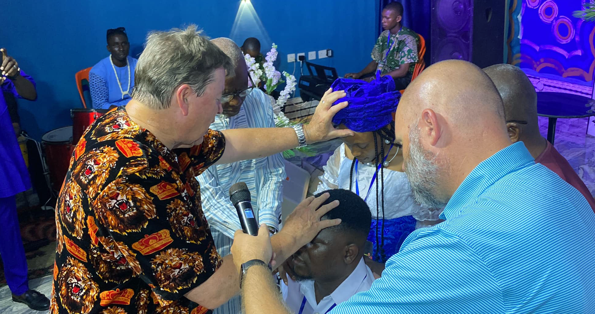 Men laying hands on people in a church service, one man is wearing a patterned shirt.