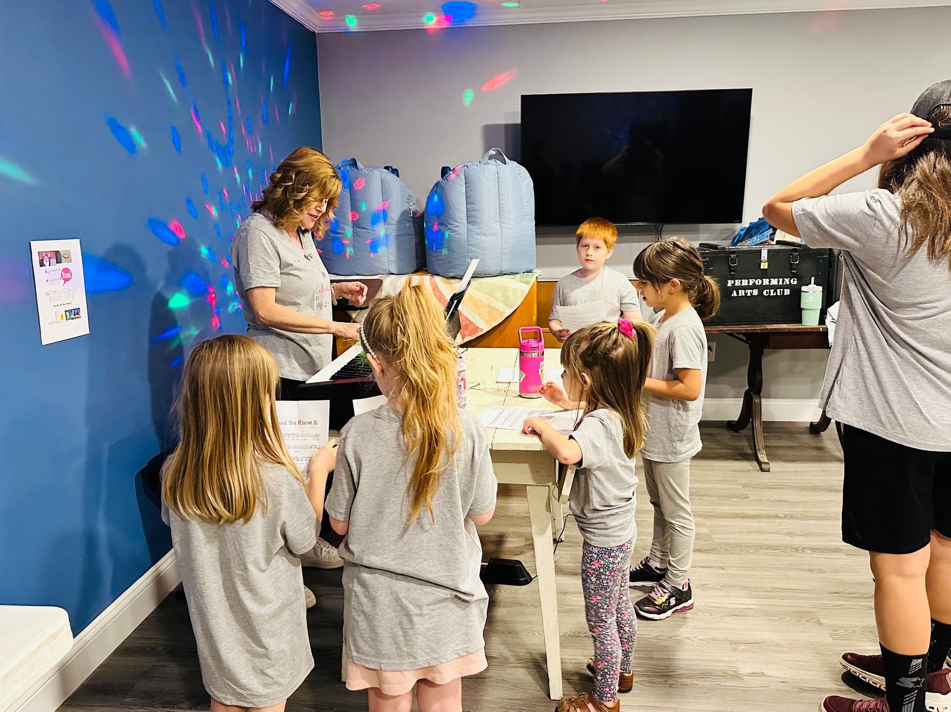 Children's activity. A woman and children gather at a table; party lights, blue wall.