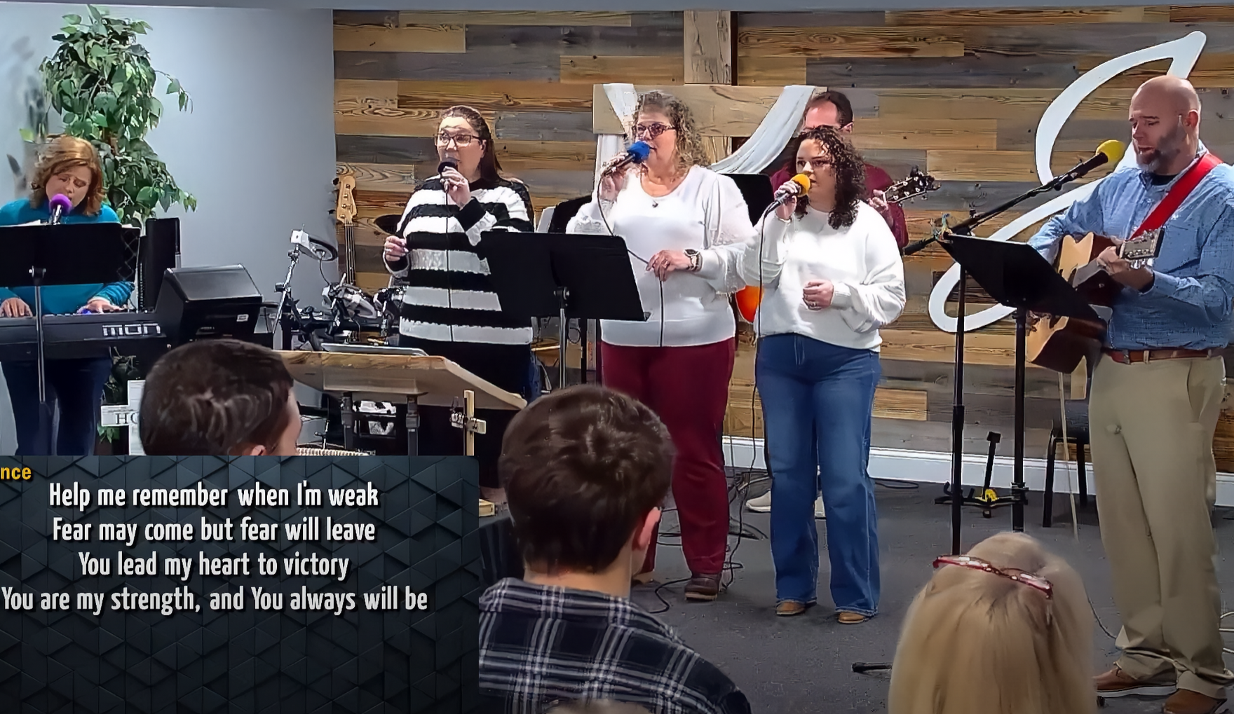A band of people singing on stage at church. A piano and guitar are visible.