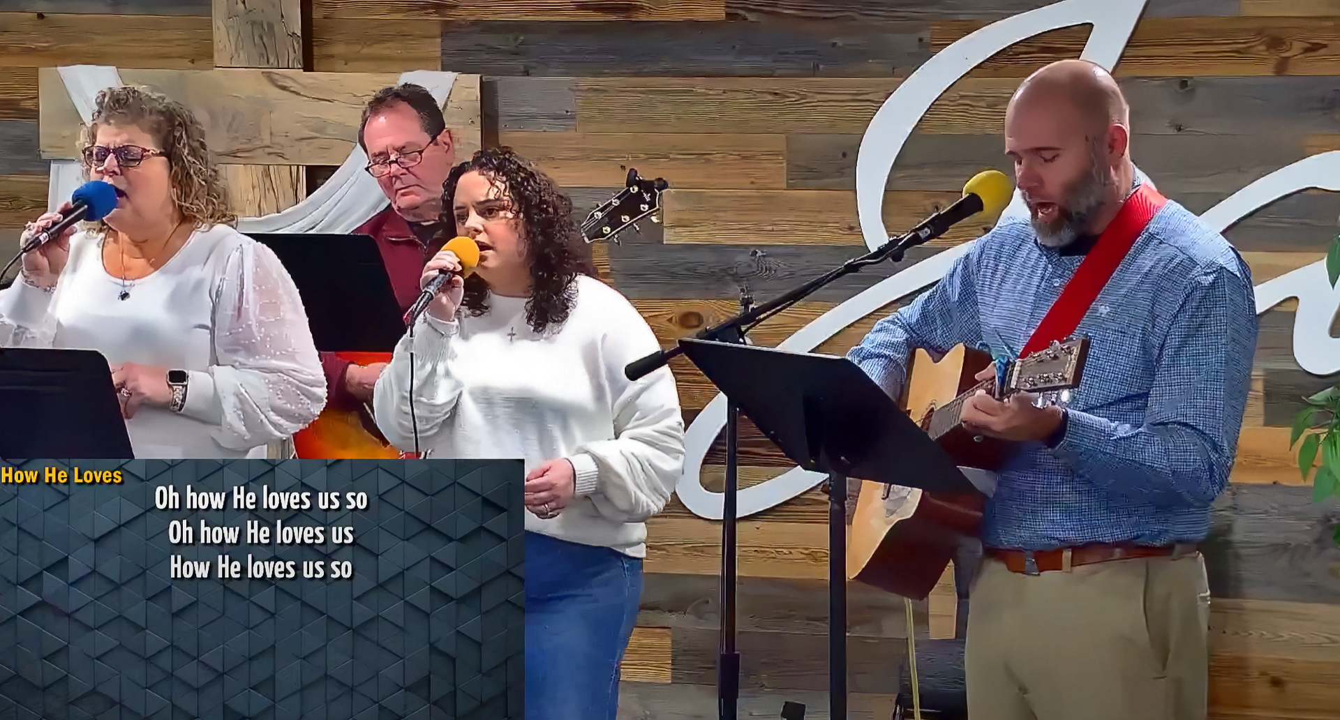 A worship band singing at church: two women, a man on guitar, and a man behind them.