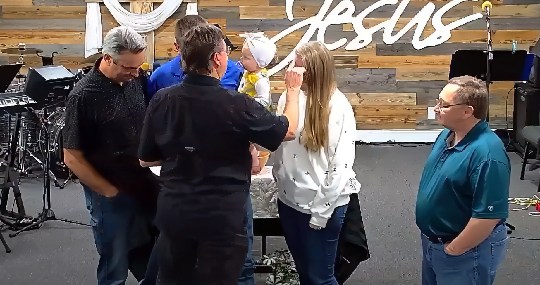 People gathered around a table in a church, someone is anointing the face of a baby.