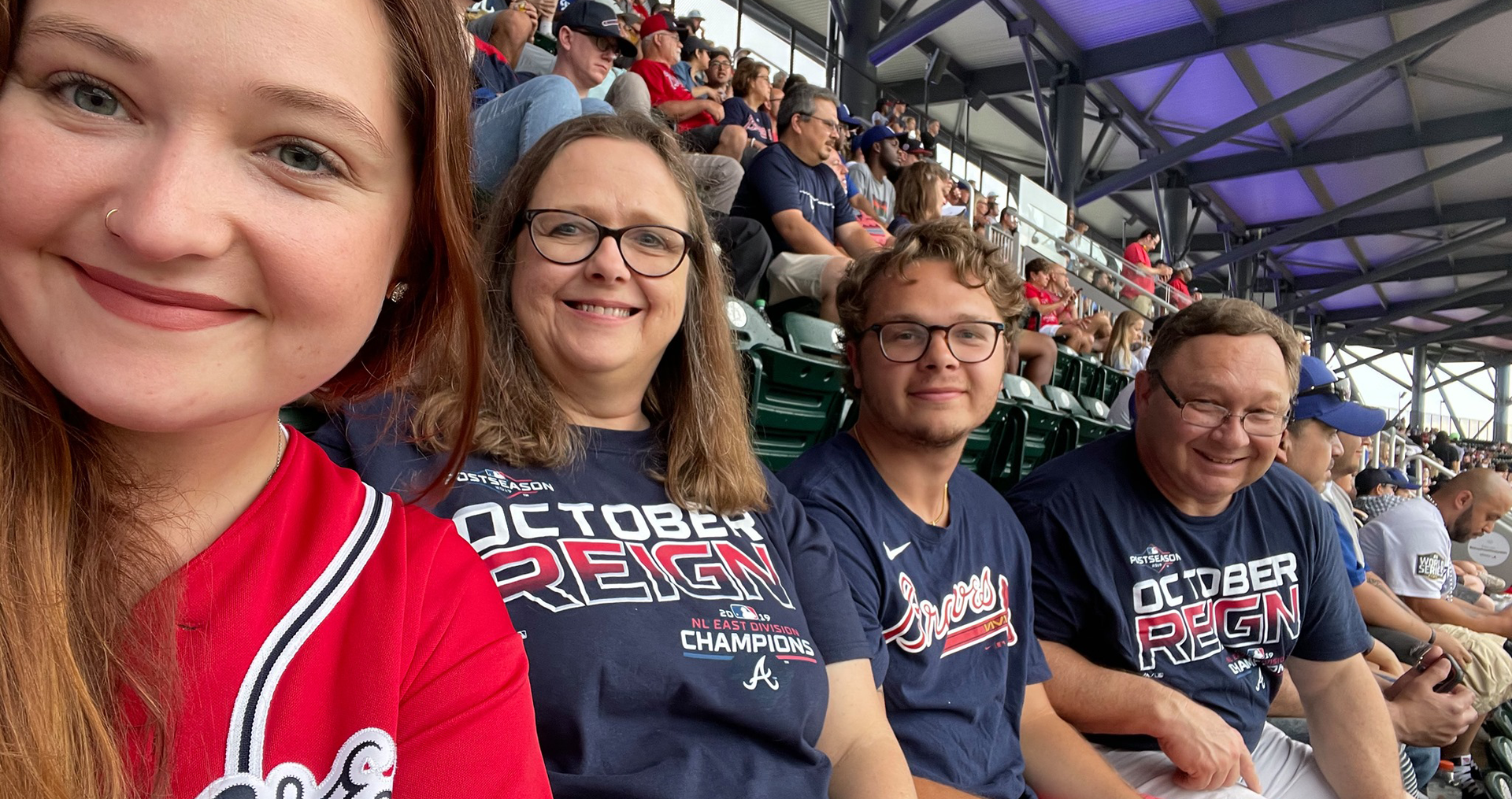 Family at a baseball game; wearing Braves shirts; smiling, in stadium seats.