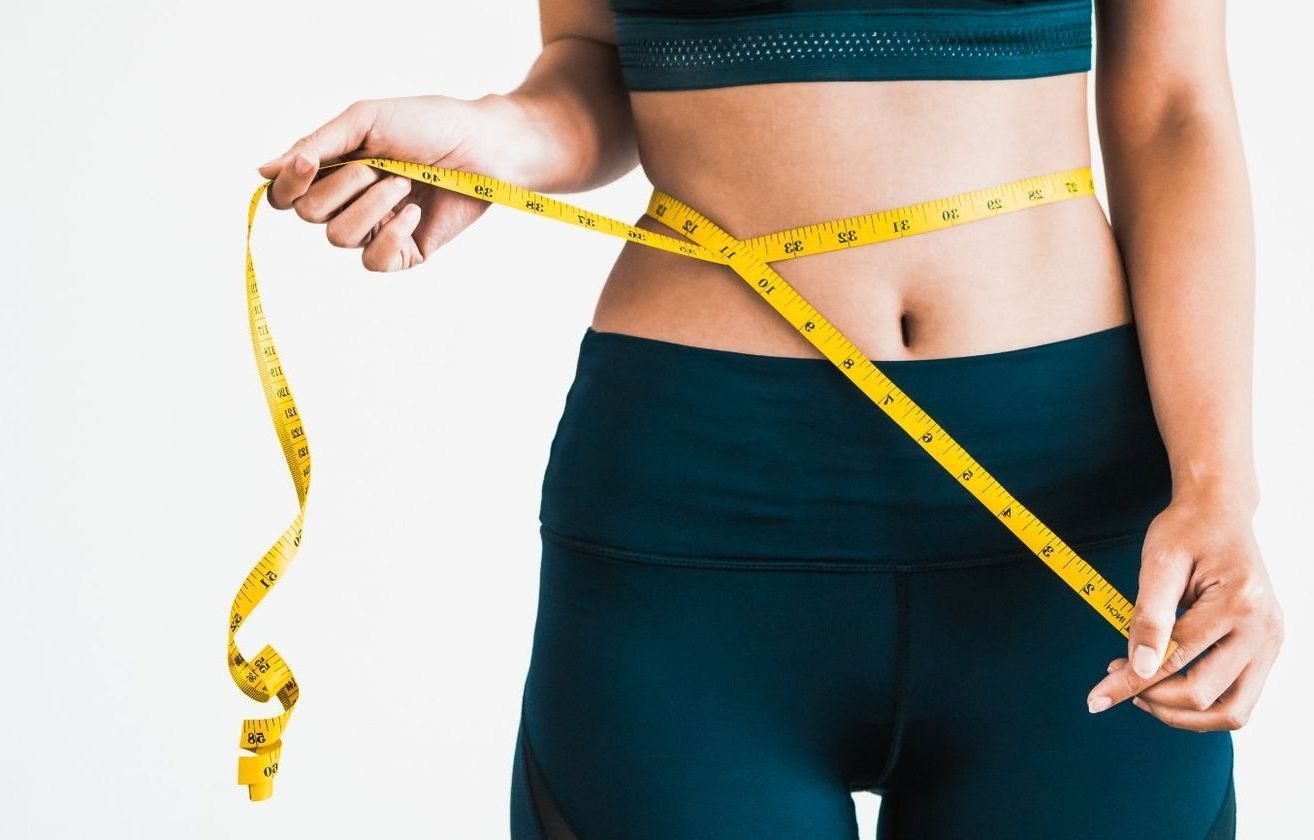 A woman is measuring her waist with a tape measure.