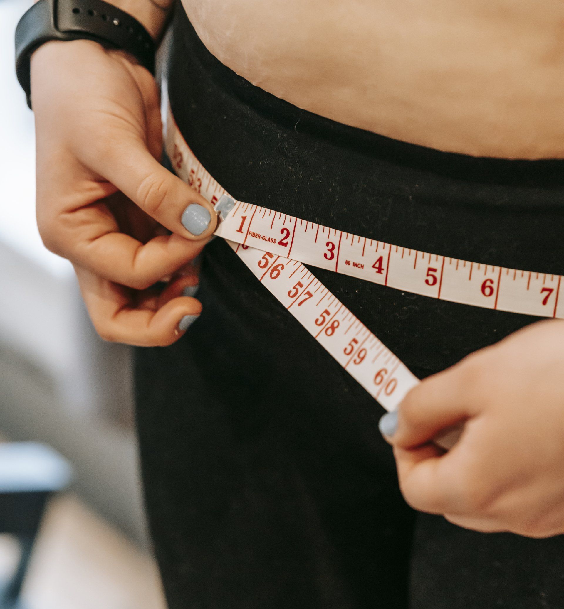 A woman is measuring her waist with a tape measure.