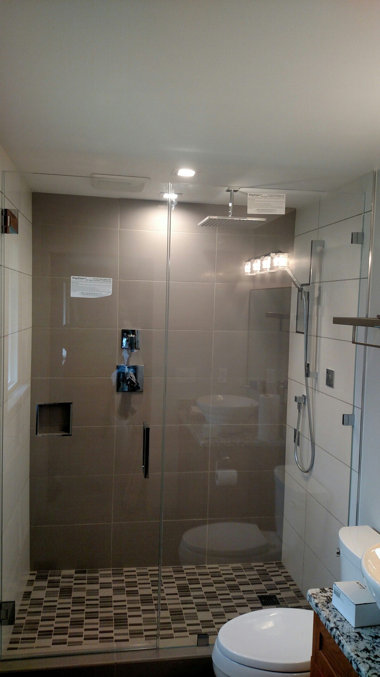 Modern bathroom with a glass shower, gray tile, and stone floor.