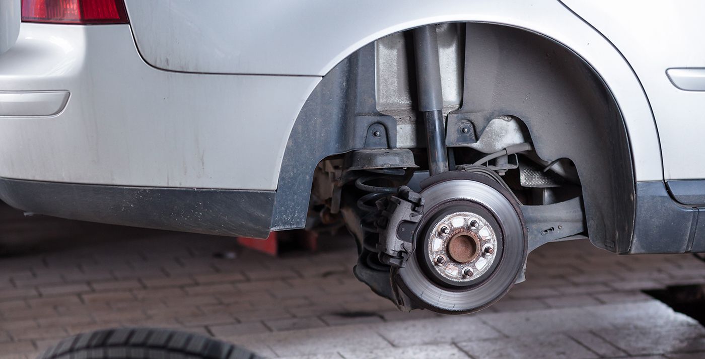 Car wheel removed, showing brake disc, suspension parts, and tire on the ground, in a garage.