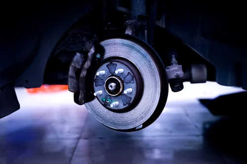 Close-up of a car's front brake rotor and caliper with a blue-lit wheel well