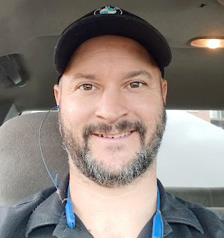 A man with a beard is sitting in a car wearing a hat and headphones.