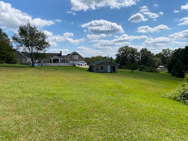 Green yard with a house and detached garage under a partly cloudy blue sky.