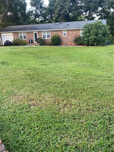 Brick ranch-style house with green lawn and trees.