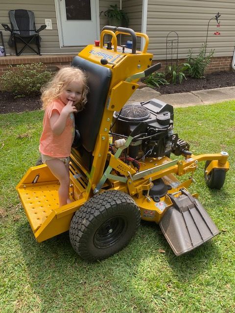 Girl standing on yellow lawnmower, outdoors.