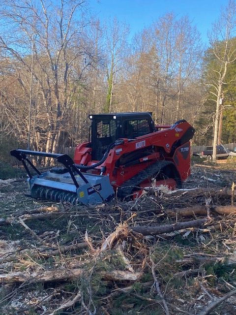 Red and black skid steer with forestry mulcher clears brush in wooded area.