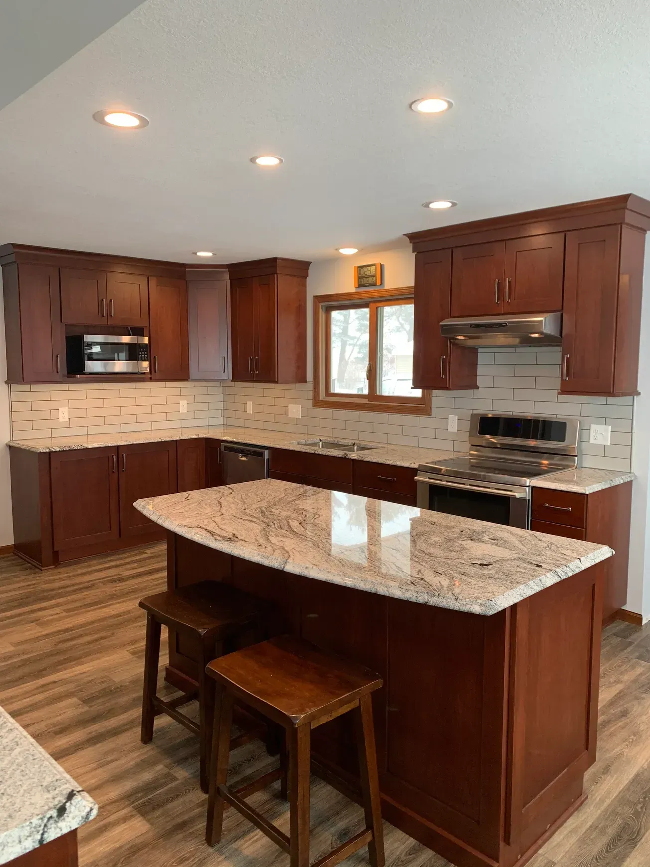 A kitchen with wooden cabinets , granite counter tops , stools and a large island.