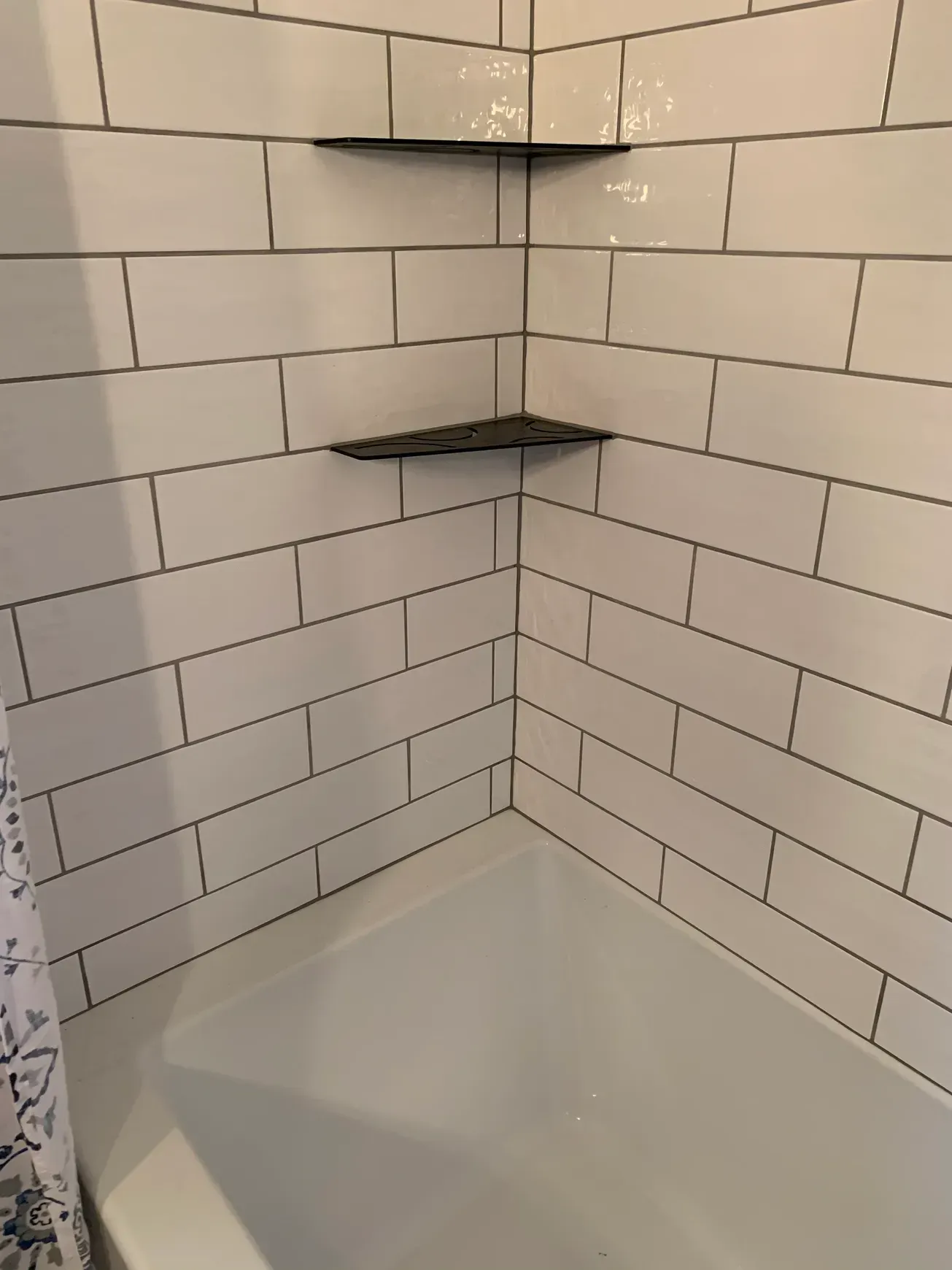 A bathroom with white brick walls and a bathtub with a shelf in the corner.