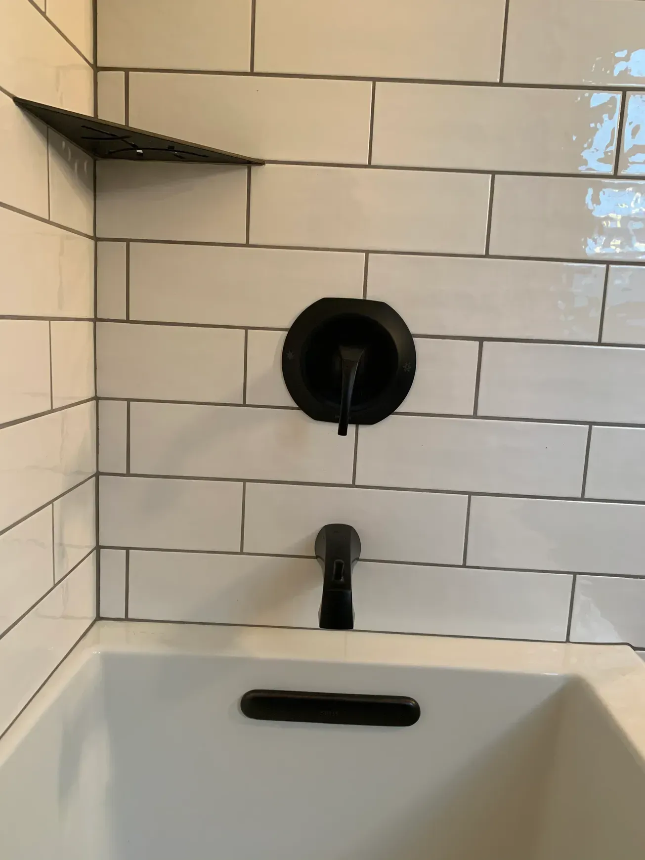 A bathtub in a bathroom with white tiles and a black faucet.
