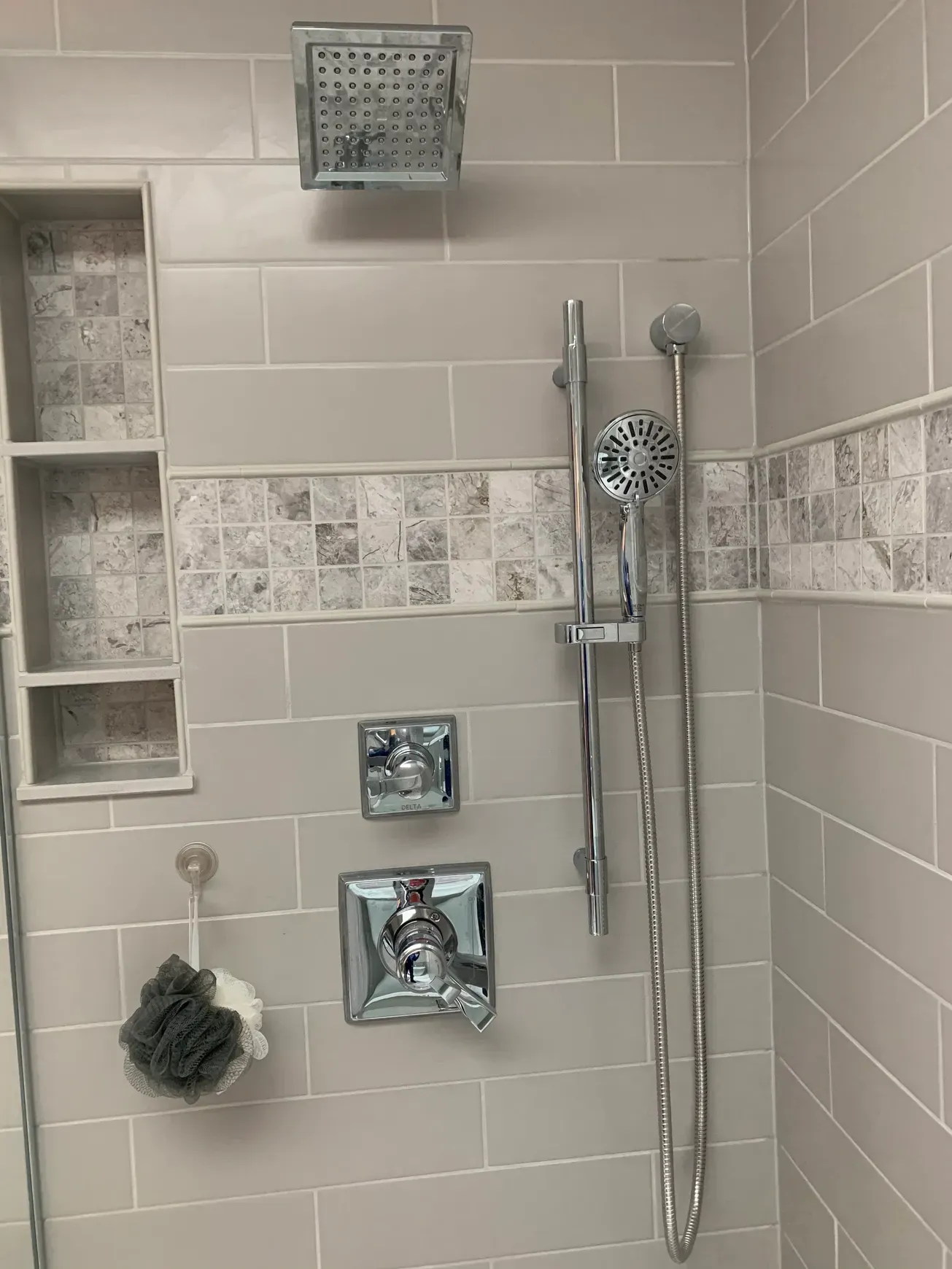 A shower with two shower heads and a sponge on the wall.