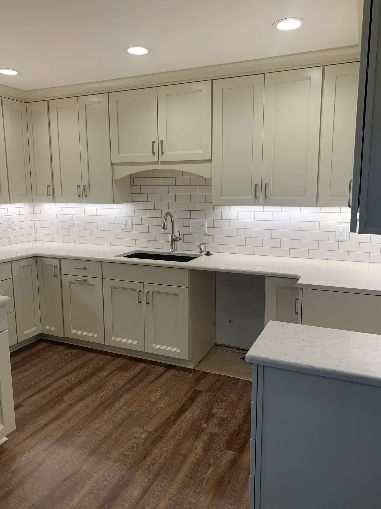 A kitchen with white cabinets , a sink , and a brick wall.