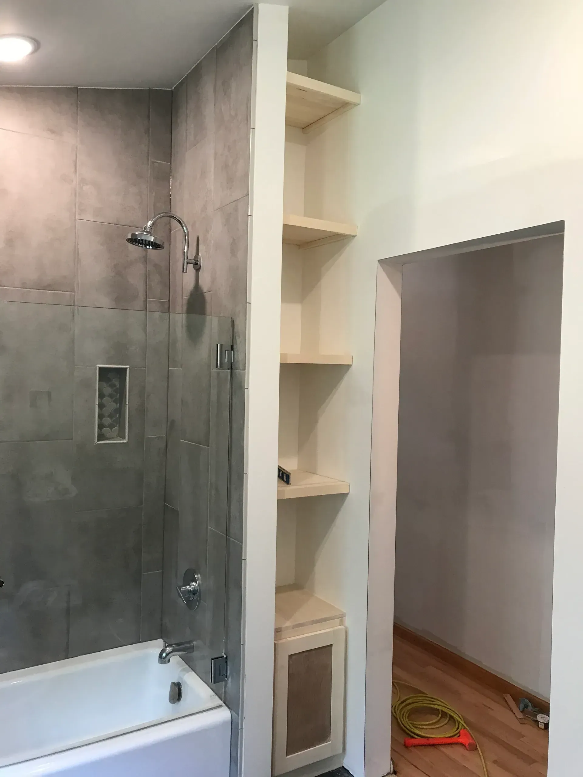 A bathroom with a bathtub , shower , and shelves.