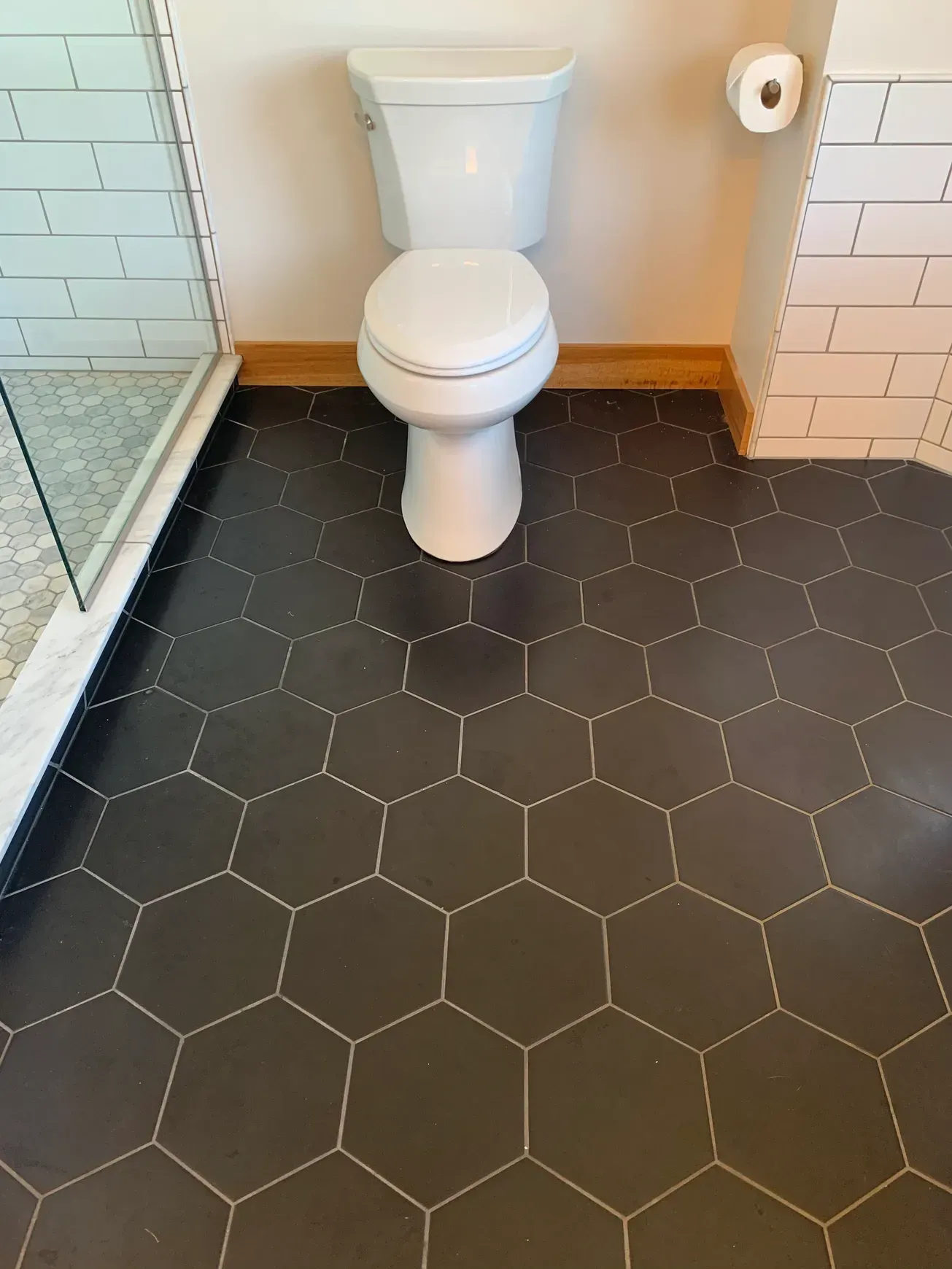 A toilet is sitting on a black tiled floor in a bathroom.