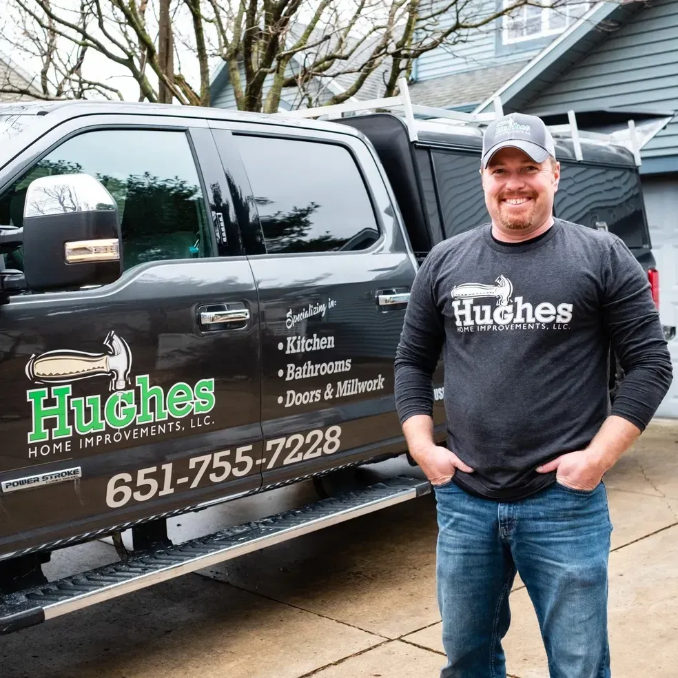 A man in a hughes shirt is standing in front of a truck.
