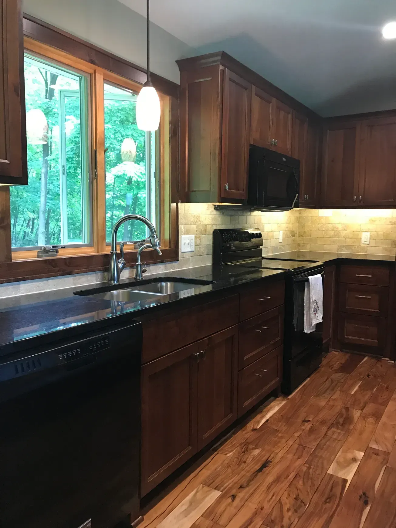 A kitchen with wooden cabinets , granite counter tops , a sink and a window.