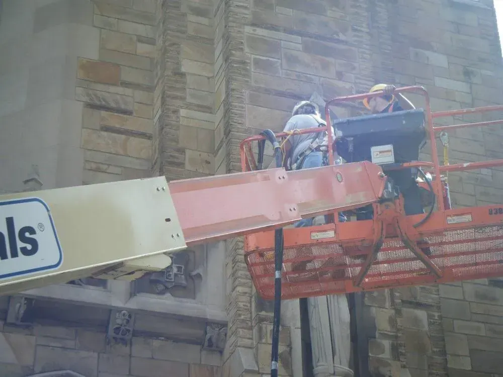 Workers on an orange lift repairing stone facade of a building.