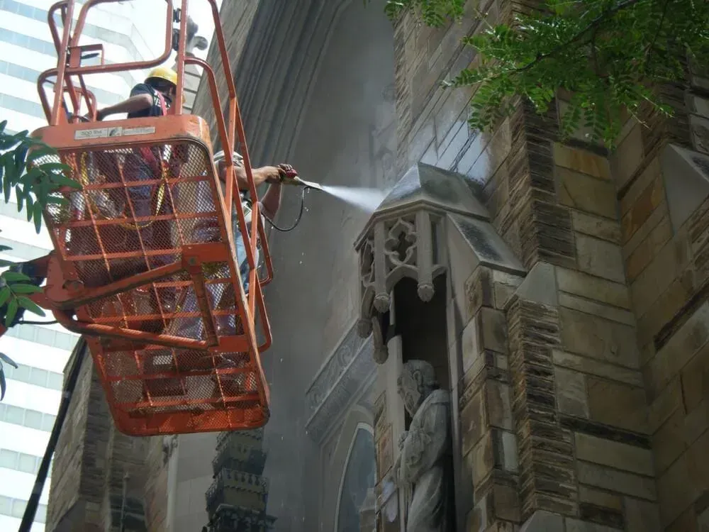 Workers on a lift washing a stone building facade with high-pressure water.
