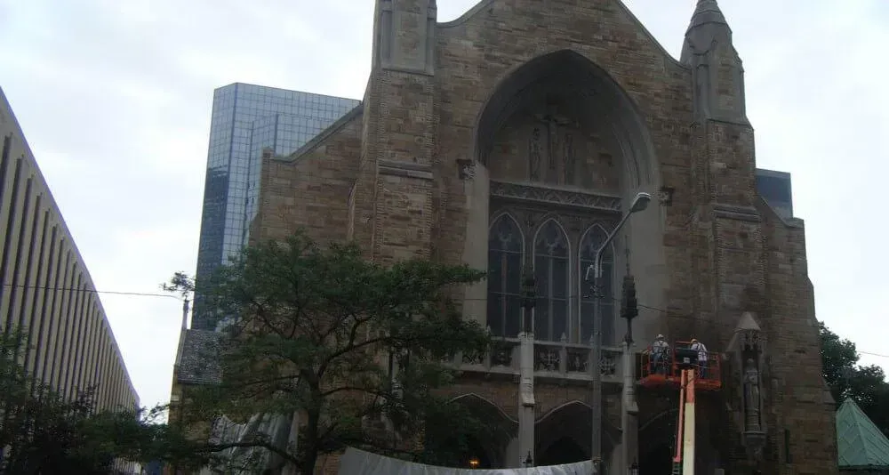 Gothic church facade with arched window, partially obscured by scaffolding, with modern buildings in background.