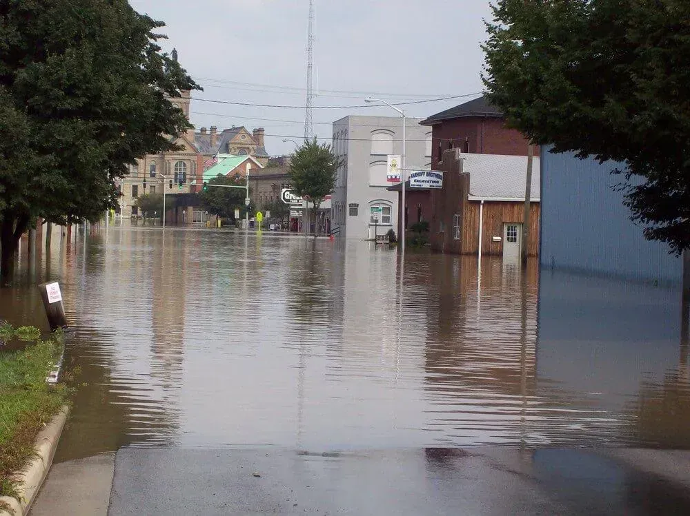 Flooded street in a town, water reaching building entrances. Overcast sky.