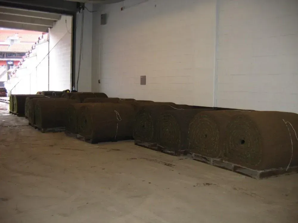 Rolls of sod on pallets inside a building, with an open doorway leading to a stadium.