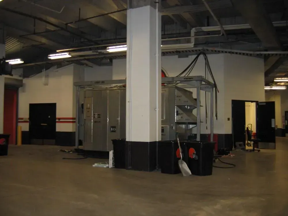 Large, empty room with a tall white pillar, metal equipment, and several black doors.