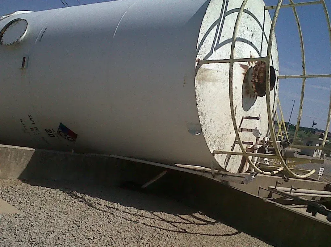 White cylindrical tank with a ladder lying on gravel.