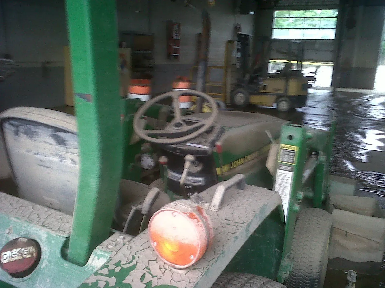 Green John Deere tractor covered in dirt, inside a garage with open doors.