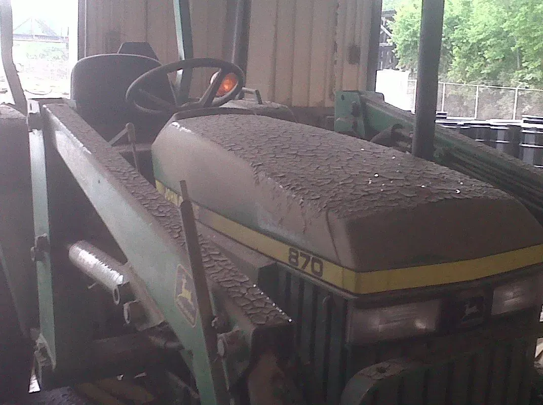 A dusty John Deere 870 tractor parked inside a shed. Green and yellow paint is visible.